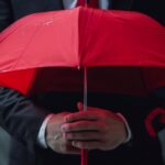 Man holding dark red umbrella signifying danger.